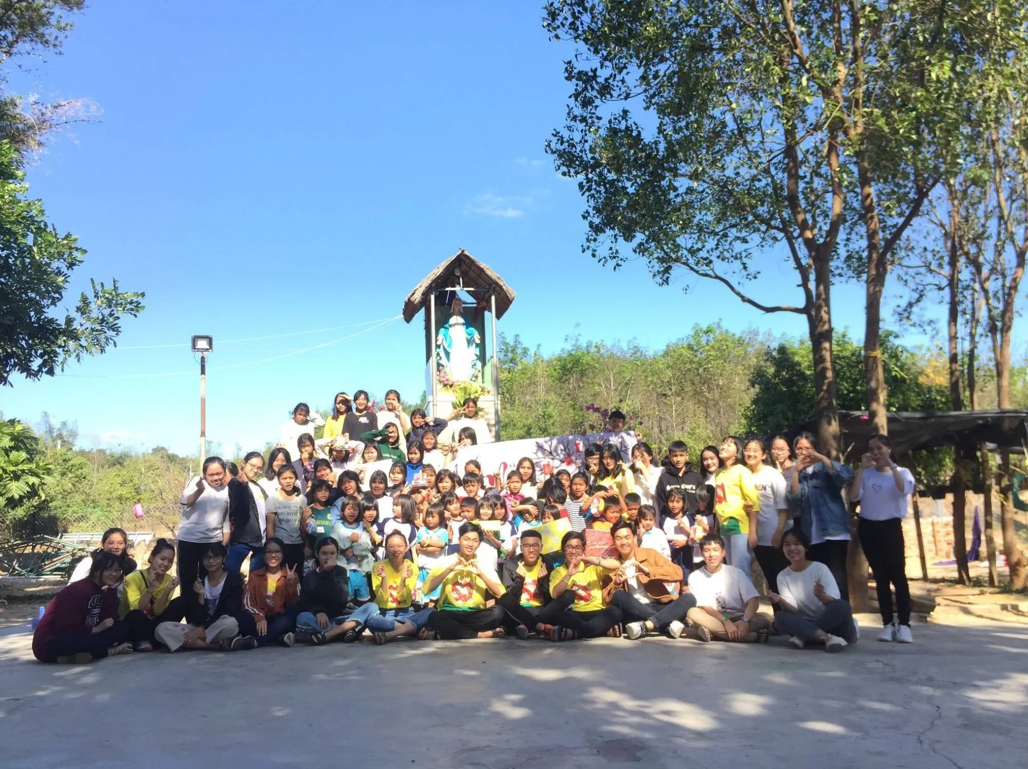 Volunteers and children of Vinh Sơn 4 together in the sunshine in front of a shrine
