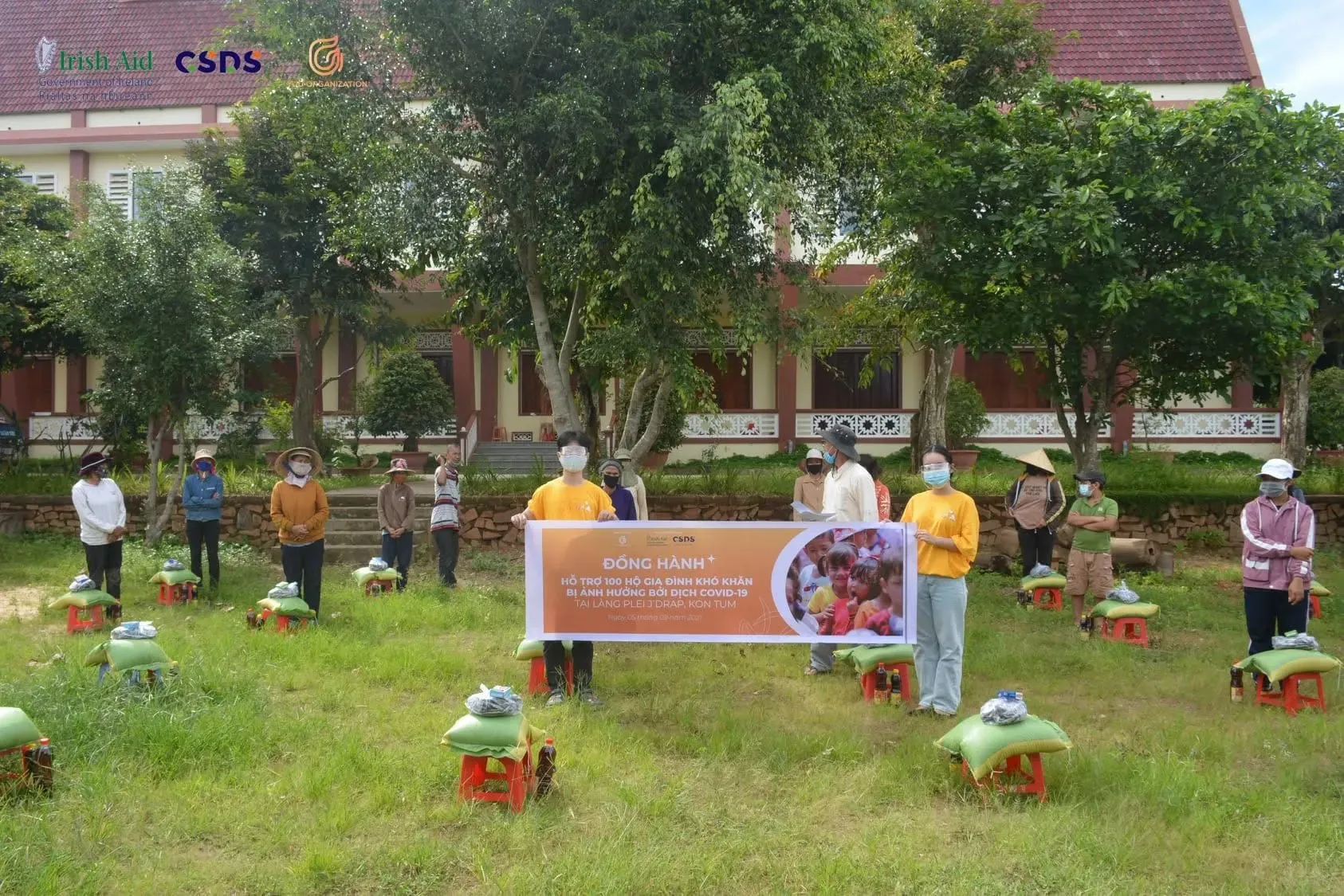 YUU volunteers holding the Đồng Hành banner among rice sacks for families in Plei J’Drap