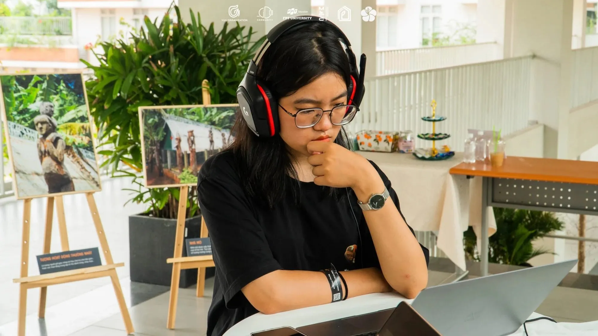 A researcher with headphones at a laptop, beside photographs of tomb house statues