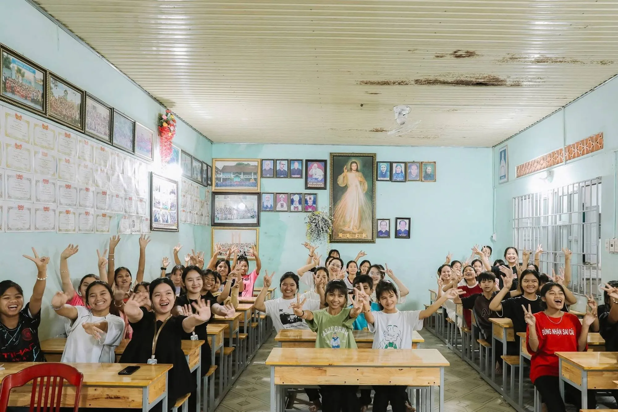 A classroom of students cheering and waving at the camera