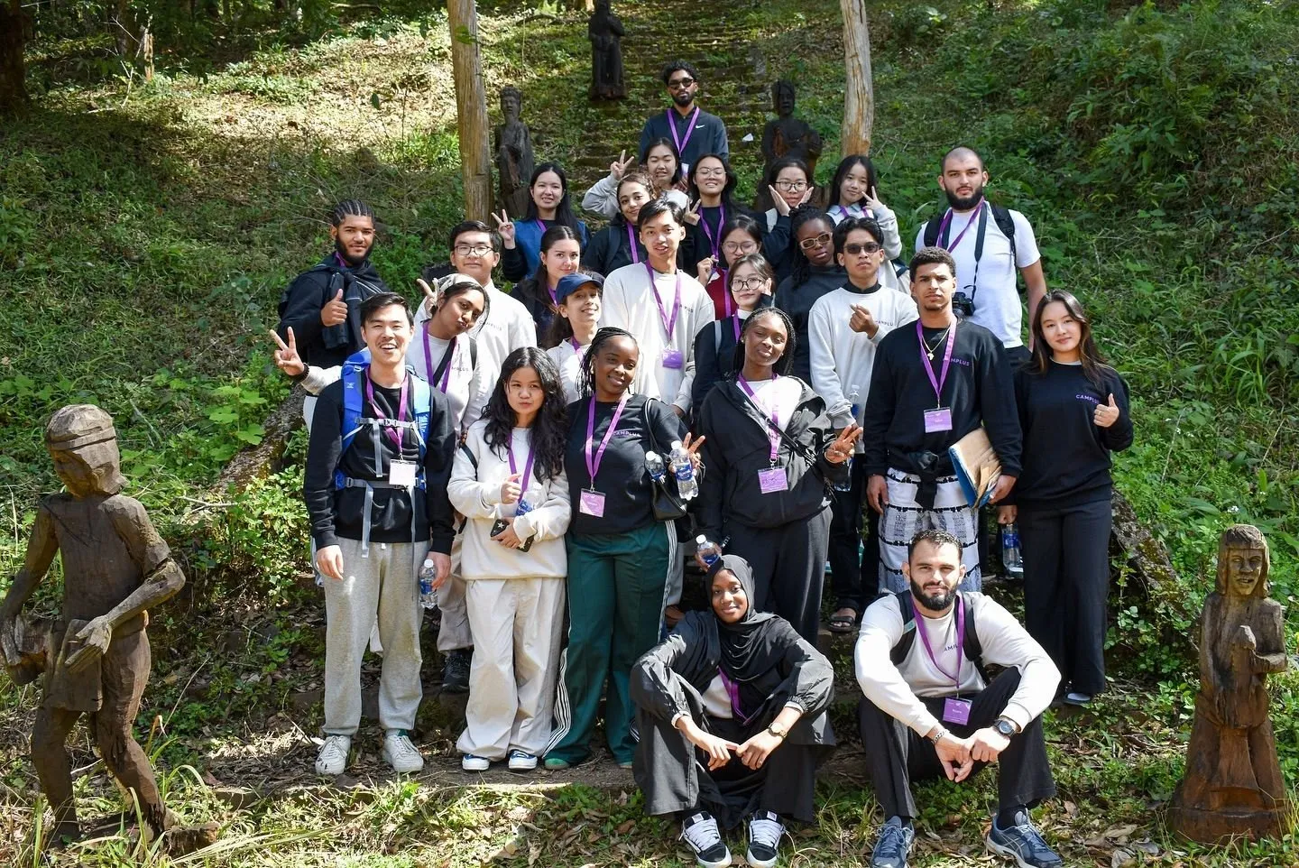 International participants of the Camplus programme among wooden tomb house statues on a forest path in Kon Tum