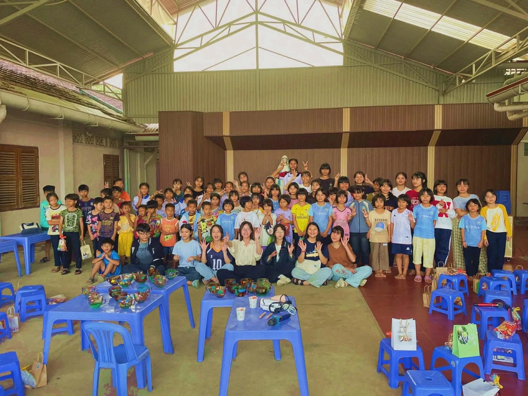 Volunteers and children together in a hall, with the glass bowls they painted on the tables