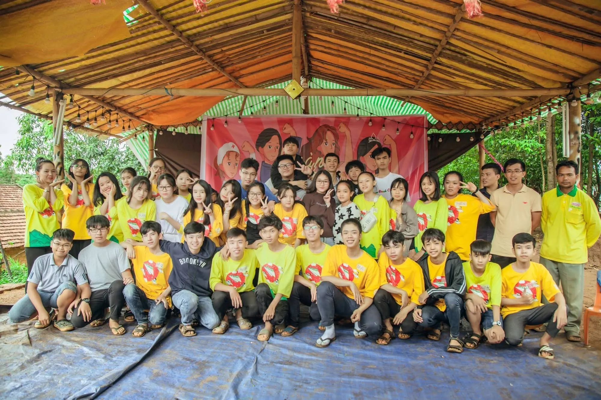 YETI students and facilitators in yellow camp shirts under a bamboo shelter